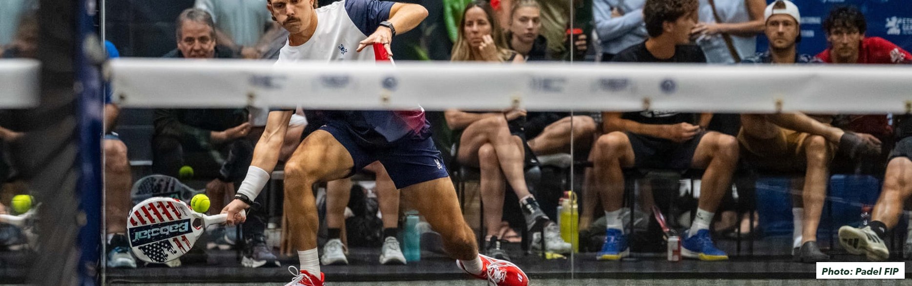 A US player stretching low for a volley at the net during the qualifier in Mississauga, the crowd watching from behind the glass