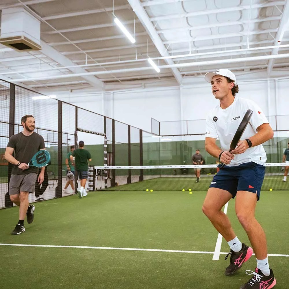 Players on the indoor green courts at The Pad Tucson, one at the net mid-point