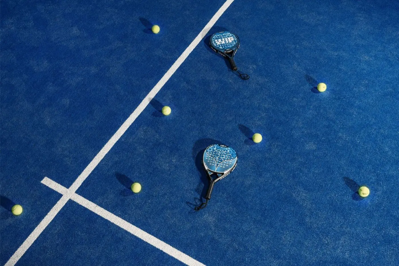 Padel rackets and balls scattered on a blue court