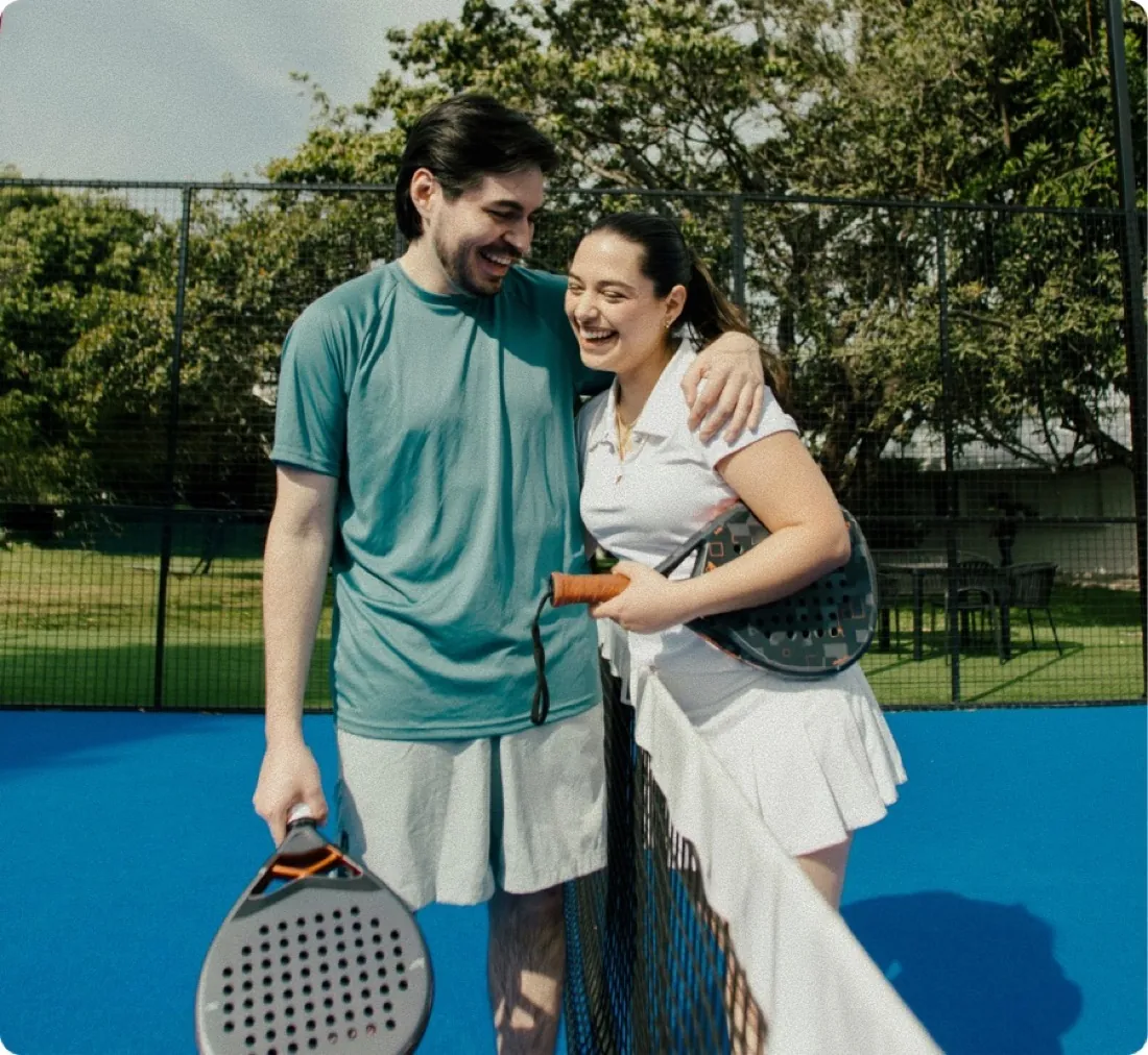 Two padel players hugging and laughing together at the net on a sunlit outdoor court.